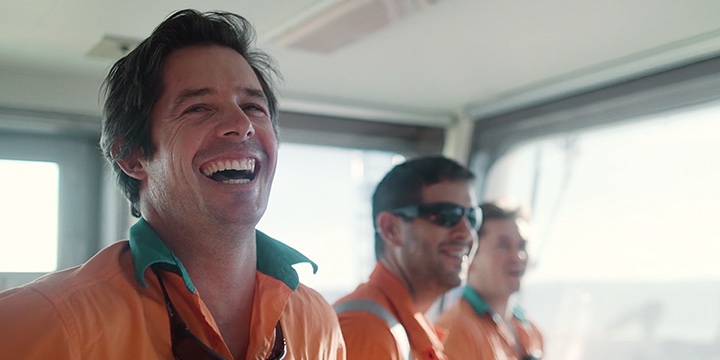 Photograph of Toll employee in uniform smiling with two other males on a boat