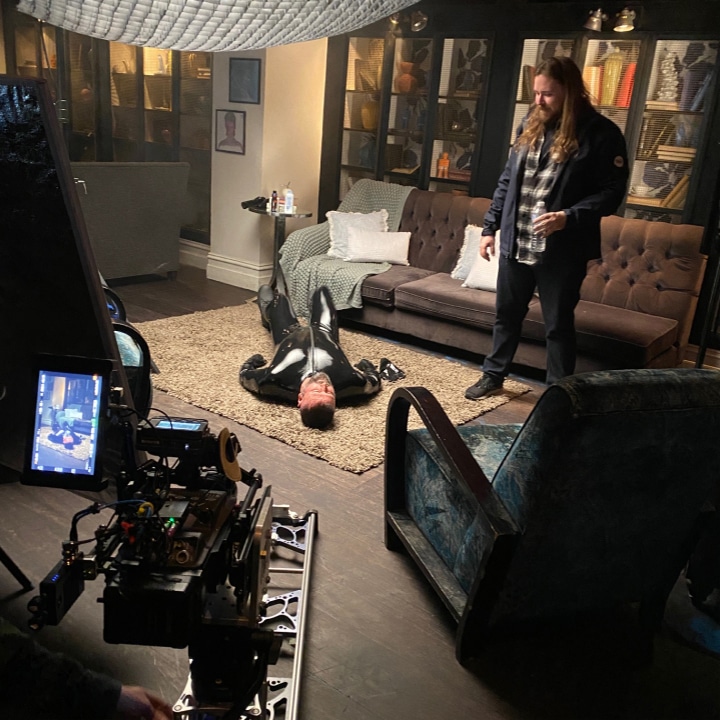 Shea standing over talent in a latex suit lying on the ground for Emen8 Monkeypox campaign.